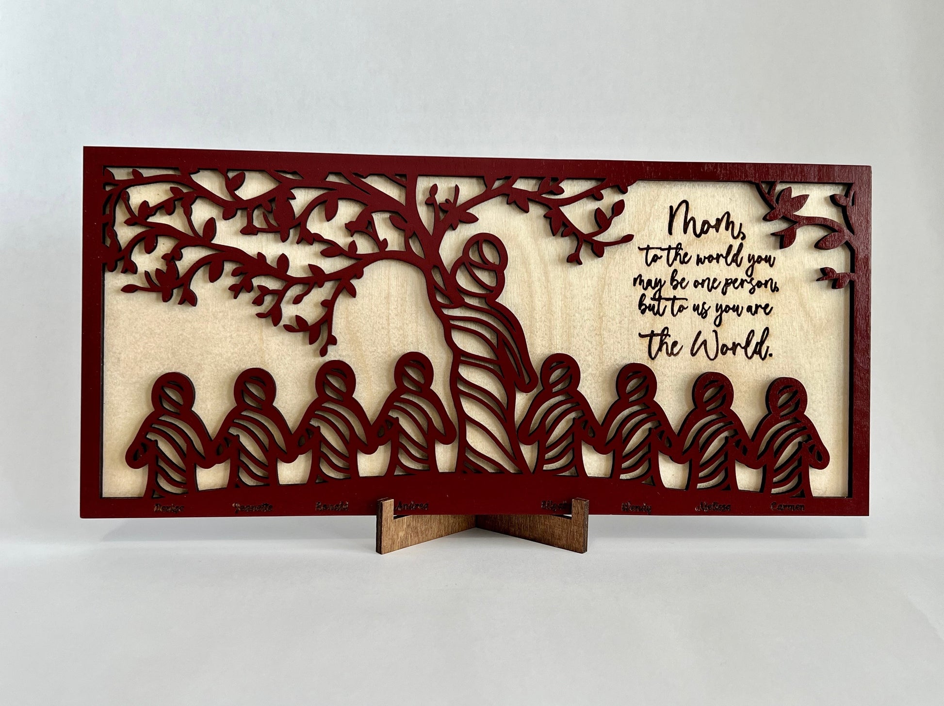 2 layered sign, top layer is red with a tree motif with a mom and 8 children represented. "Mom, to the world you may be one person, but to us you are the world."