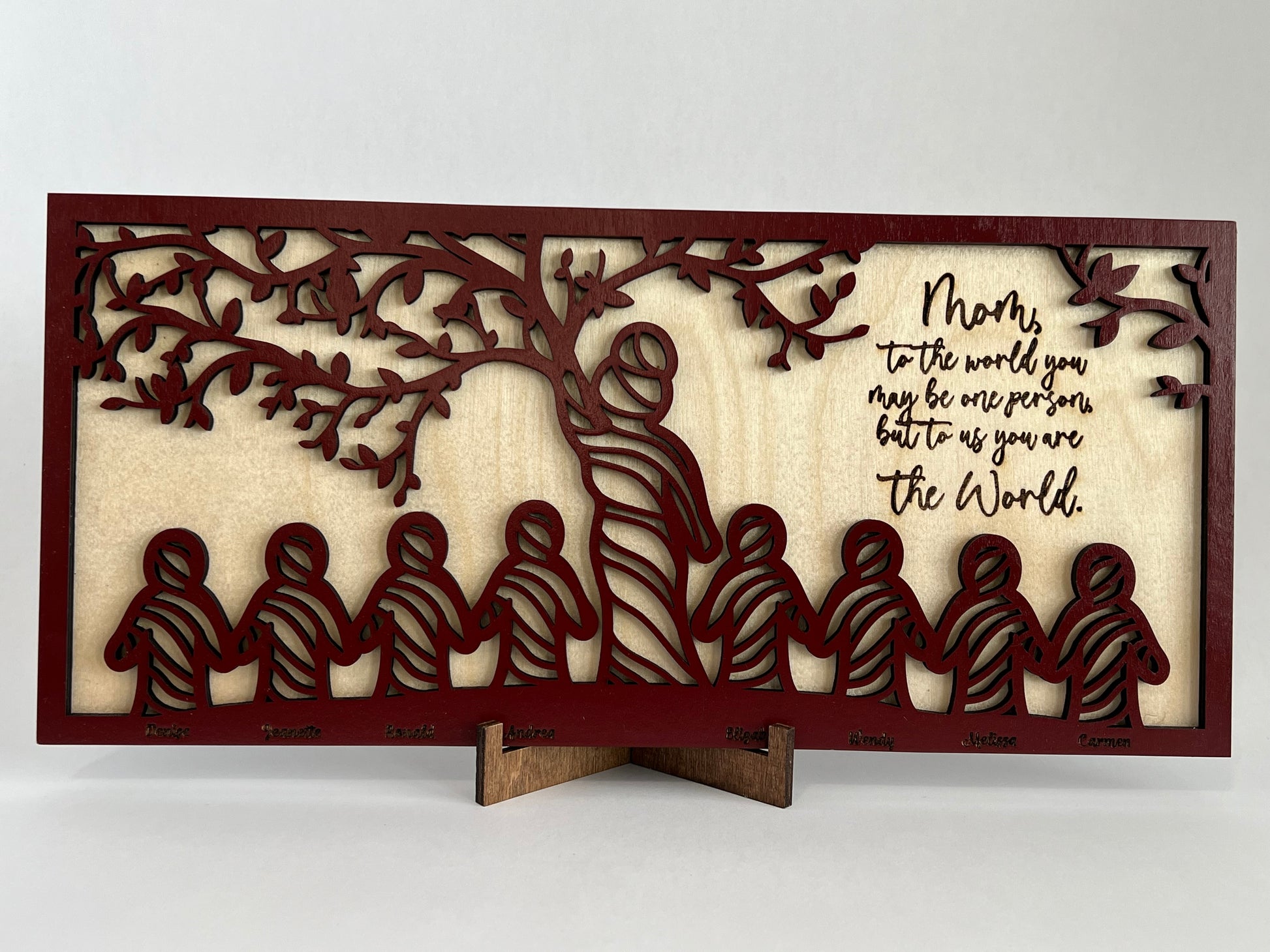 2 layered sign, top layer is red with a tree motif with a mom and 8 children represented. "Mom, to the world you may be one person, but to us you are the world."