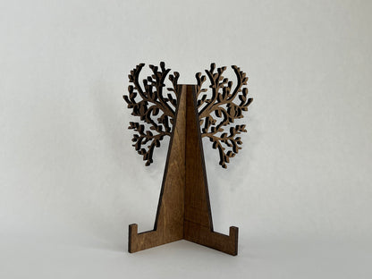 Stand for the sign, with tree branches and leaves protruding from the back of the stand, stained a warm chestnut color